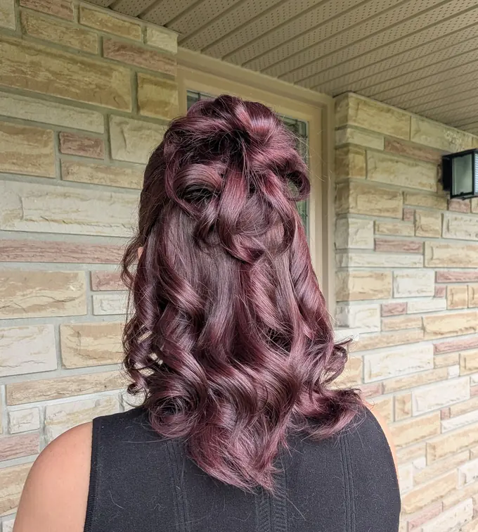 Long plum-burgundy hair curled and pinned half up, seen from behind.